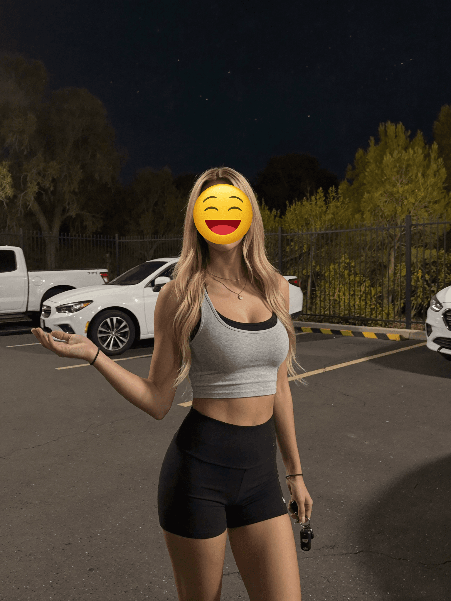 A woman in athletic wear stands outdoors at night with a playful expression.