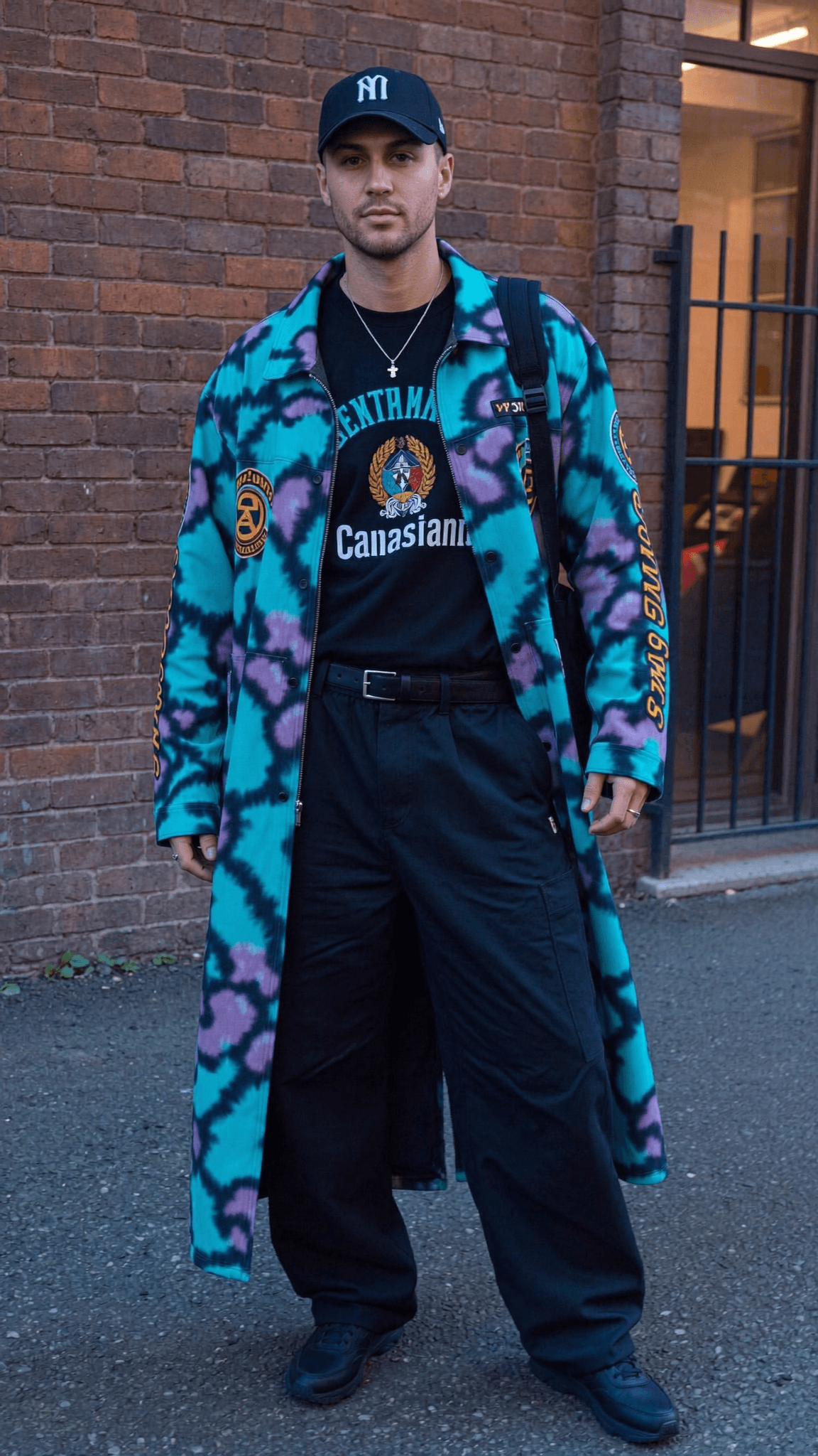 A person stands on a street wearing casual clothing with a relaxed pose.