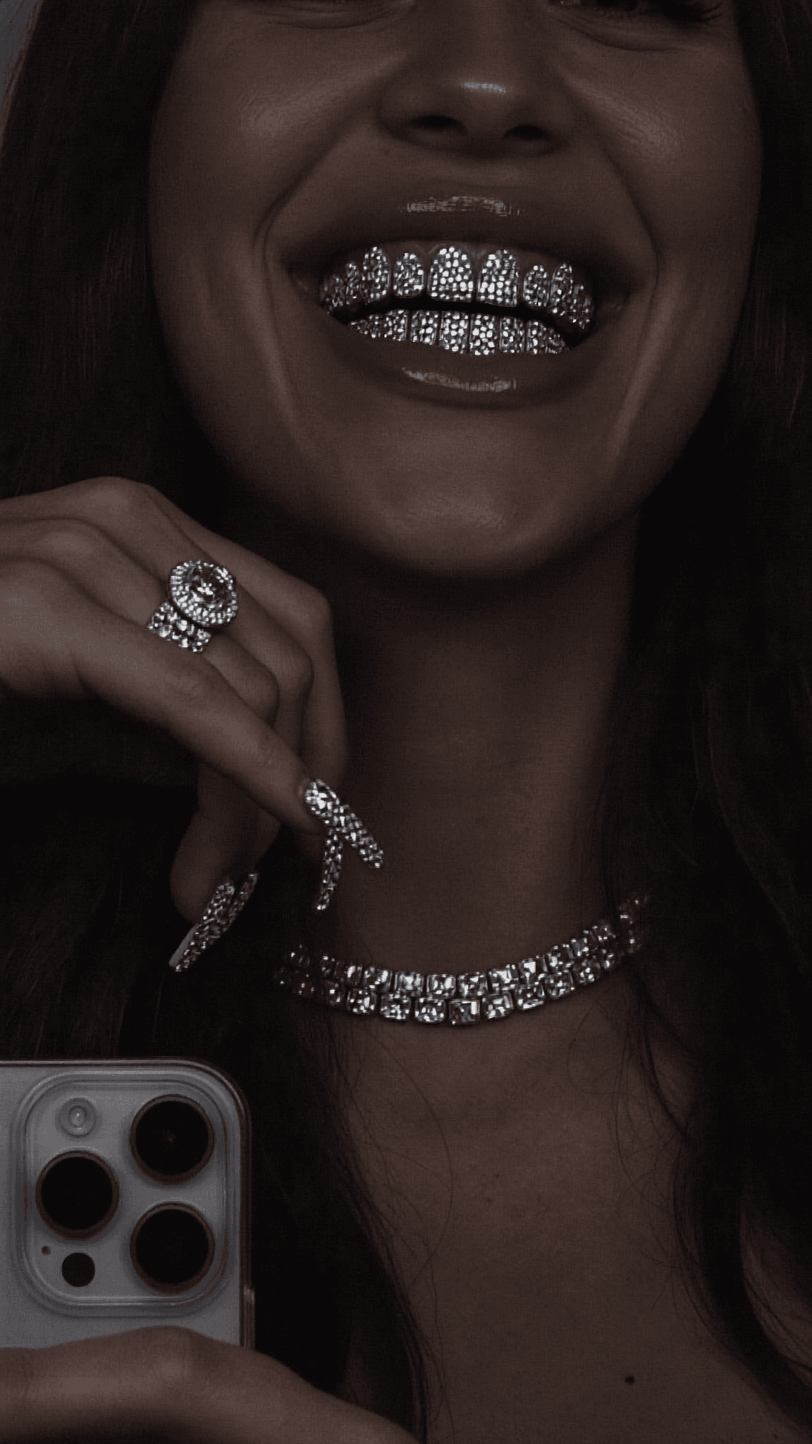 A person with a septum ring and diamond-studded teeth poses for the camera, wearing minimal jewelry.