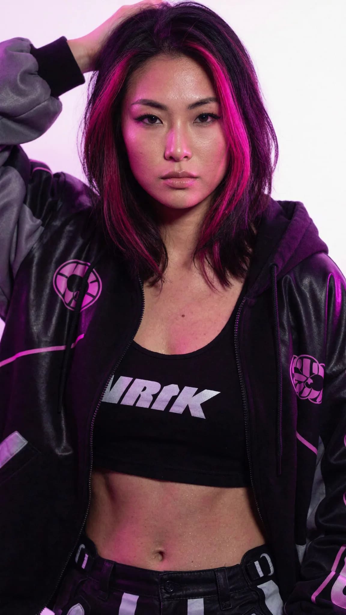 A Korean-American woman with a pixie cut and septum ring poses confidently in an athleisure outfit.