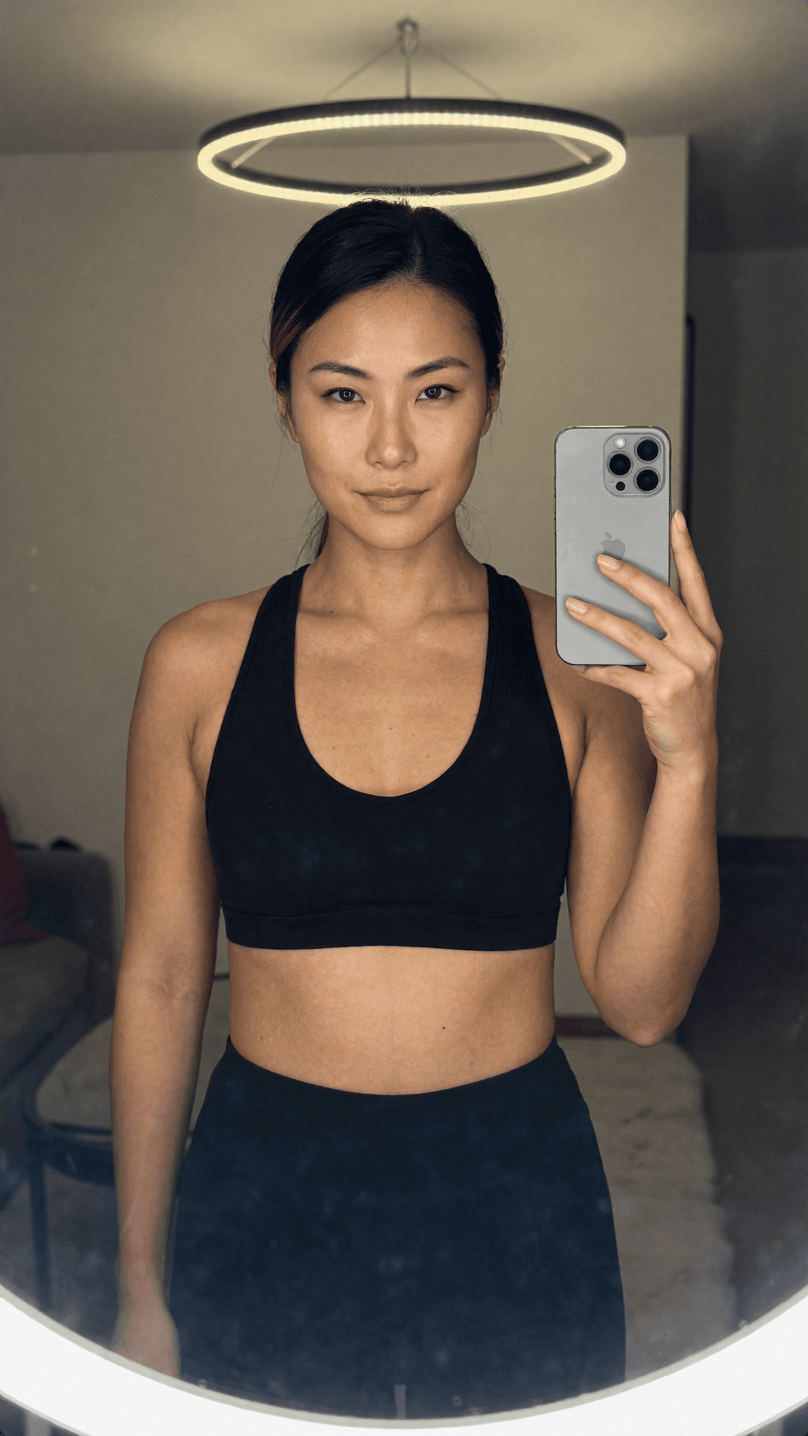 A woman in a black sports bra and leggings takes a mirror selfie, showcasing her athletic attire.