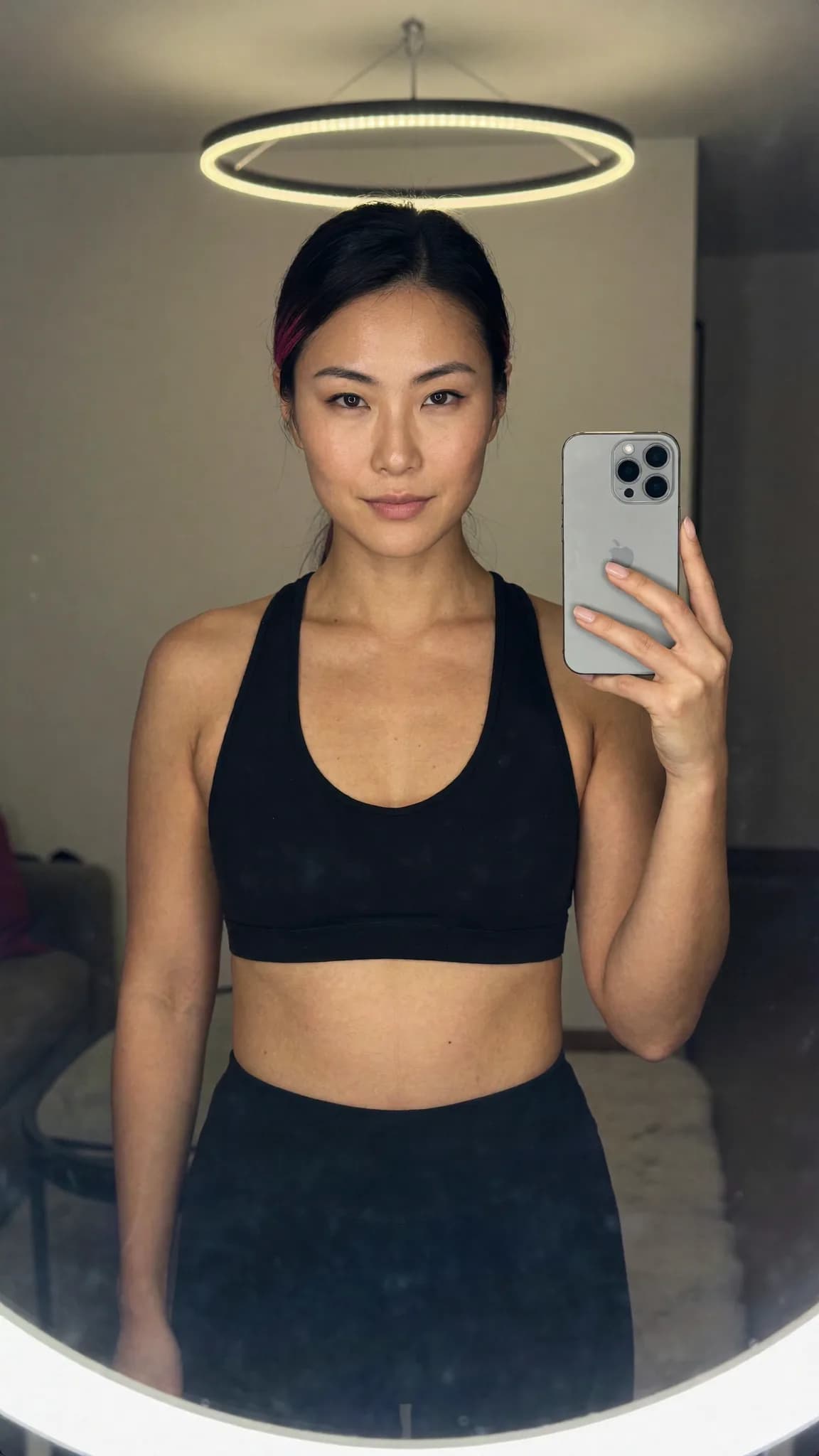 A woman in a black sports bra and leggings takes a mirror selfie, showcasing her athletic attire.