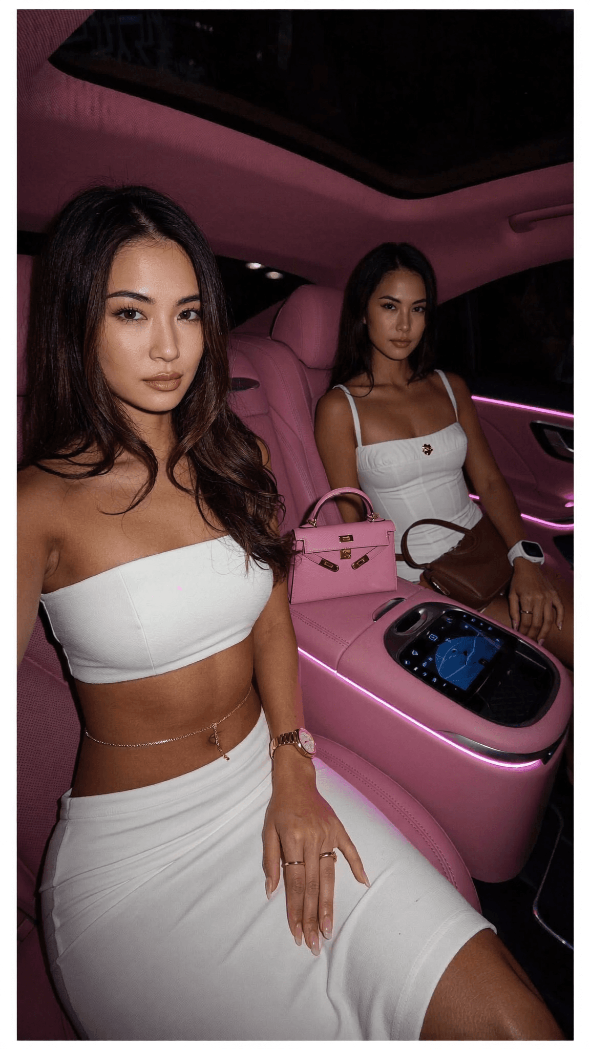 Two women in white dresses sit inside a pink car, exuding confidence and style.