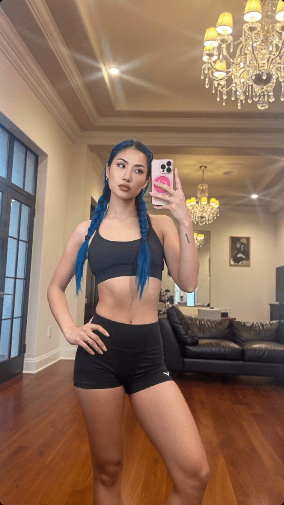 A woman with blue braided hair poses in a stylish athleisure outfit in an elegant room.