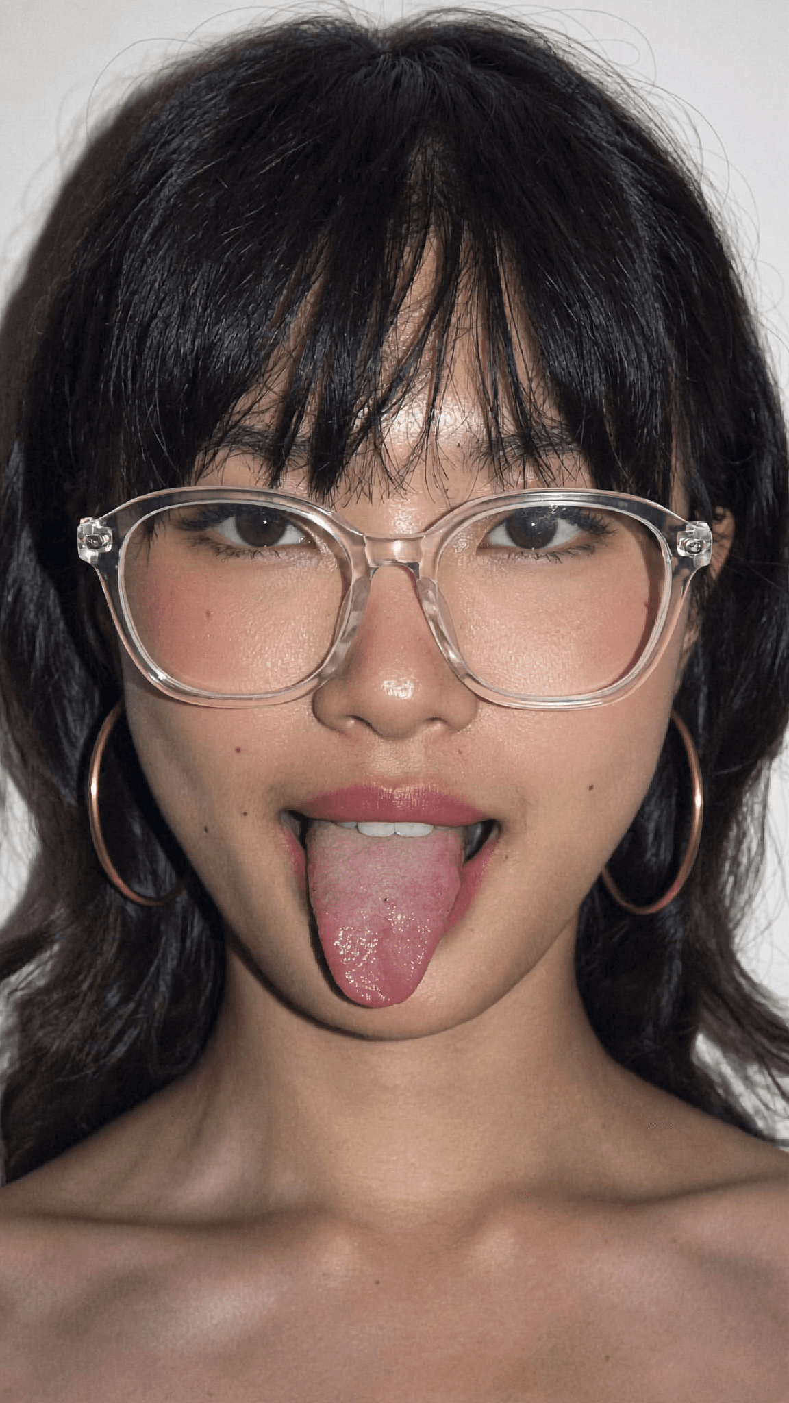 A woman with black hair and glasses is posing in a studio setting, wearing minimal clothing.