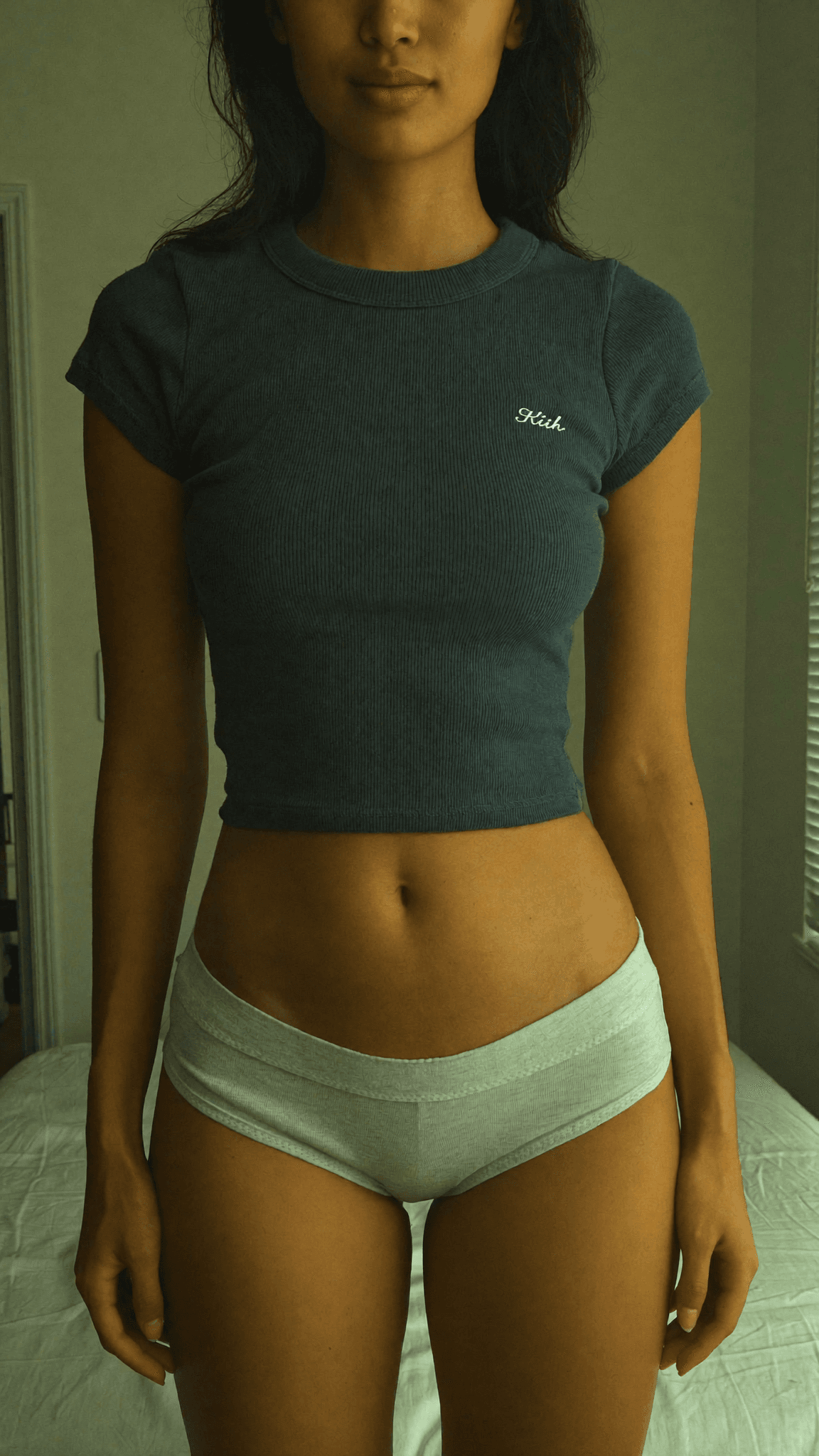 A person wearing intimate clothing stands in a bedroom setting.