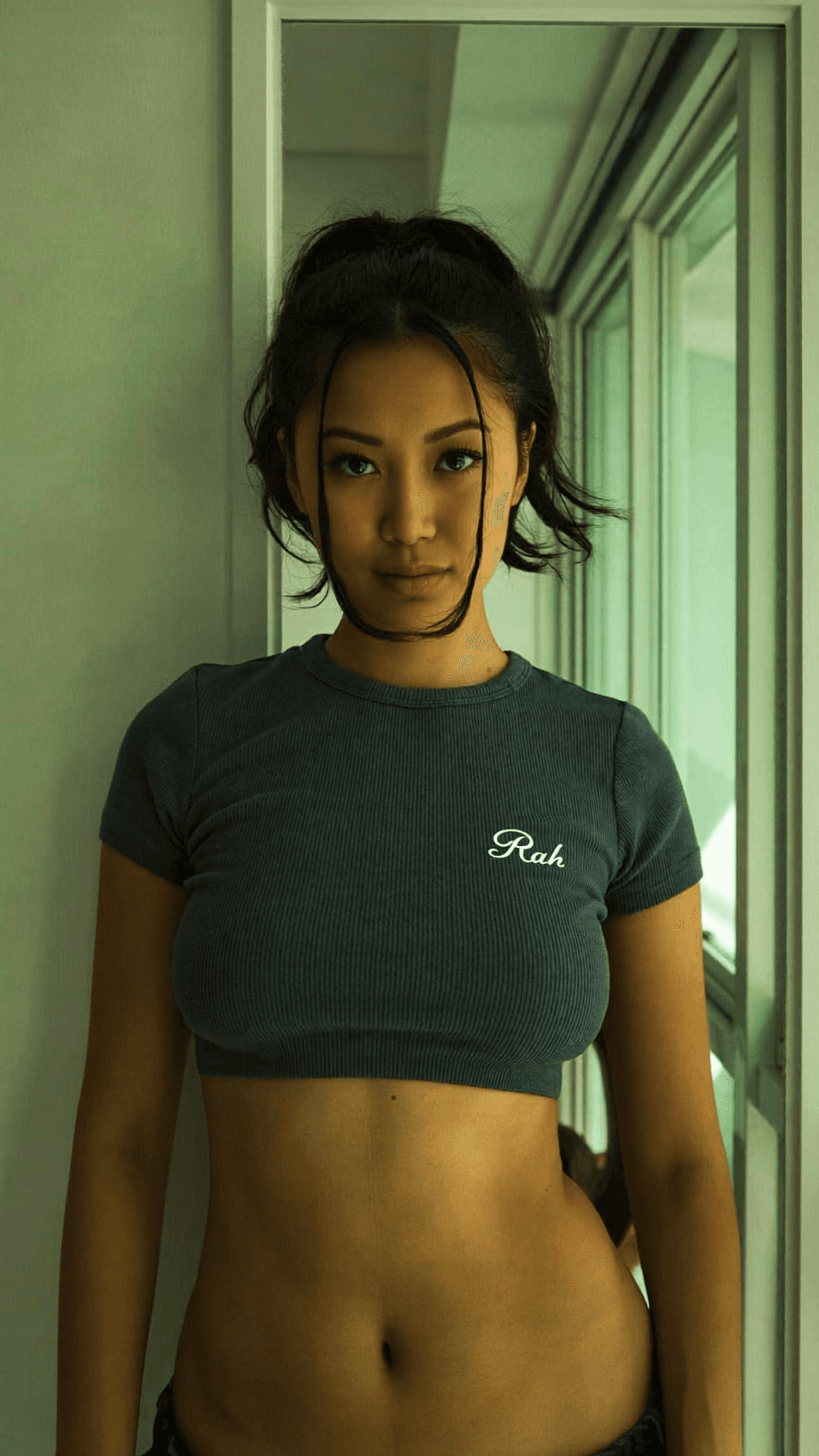 A woman in a bedroom wearing intimate attire poses for the camera.