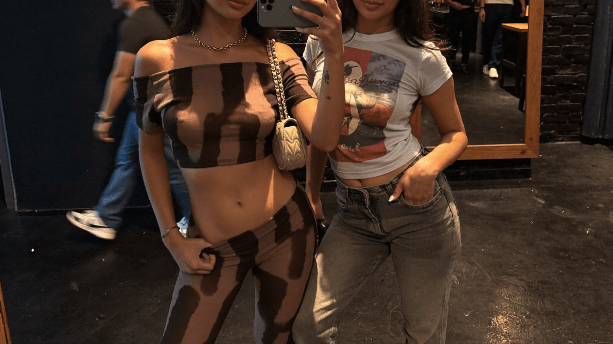 Two individuals pose for a mirror selfie in casual attire at a club.