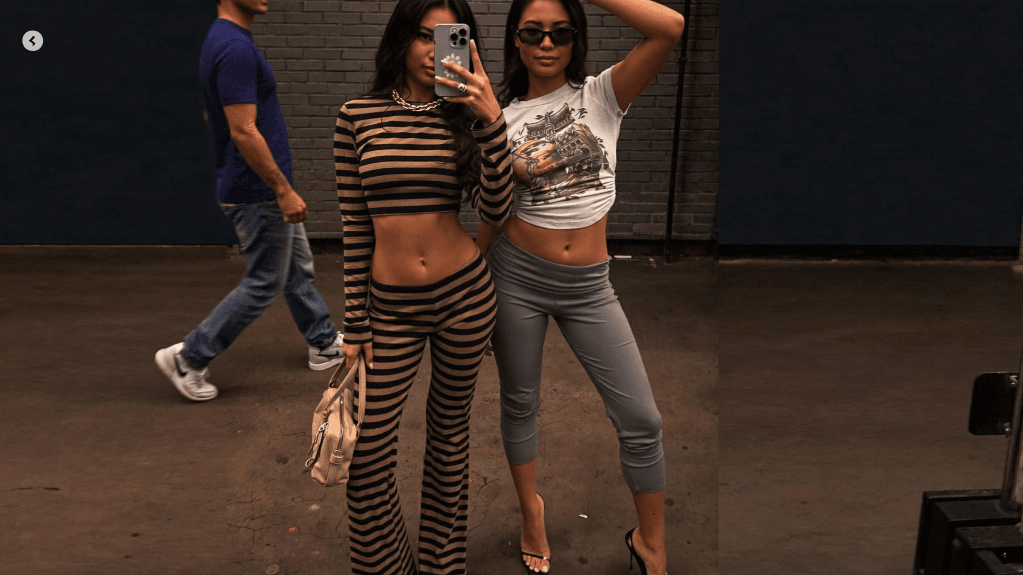 Two women pose confidently on a city street, one wearing casual attire and the other in a striped outfit.