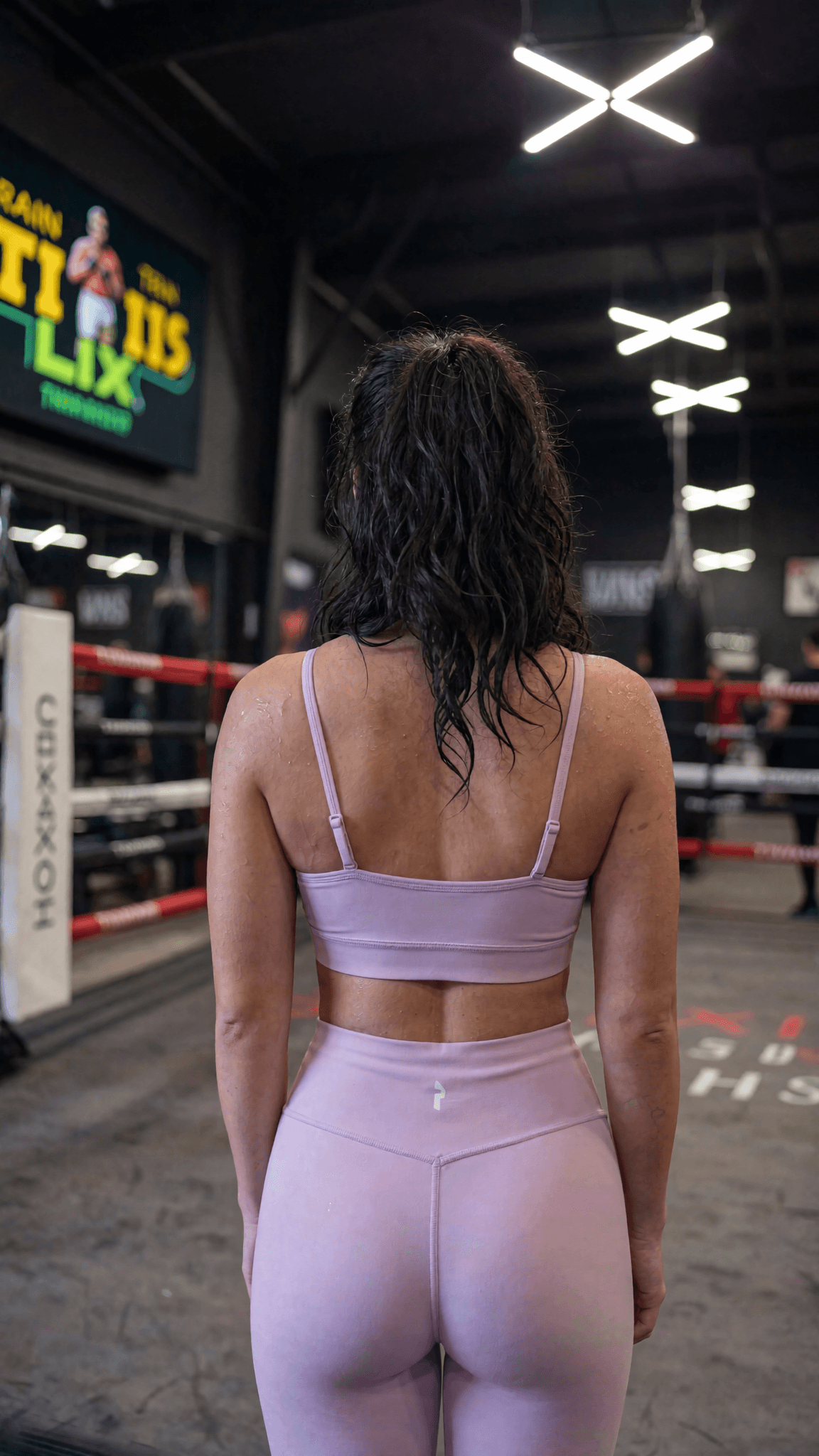 A woman in a pink athleisure outfit stands confidently in a studio setting.