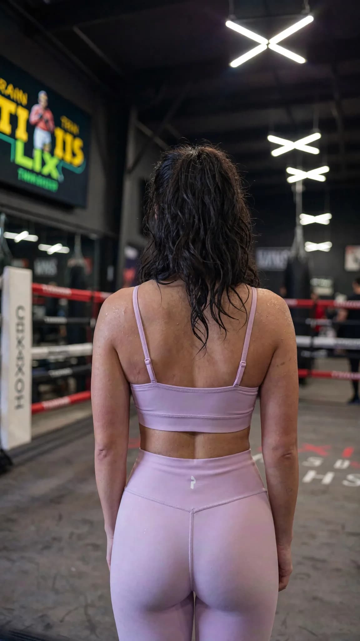 A woman in a pink athleisure outfit stands confidently in a studio setting.