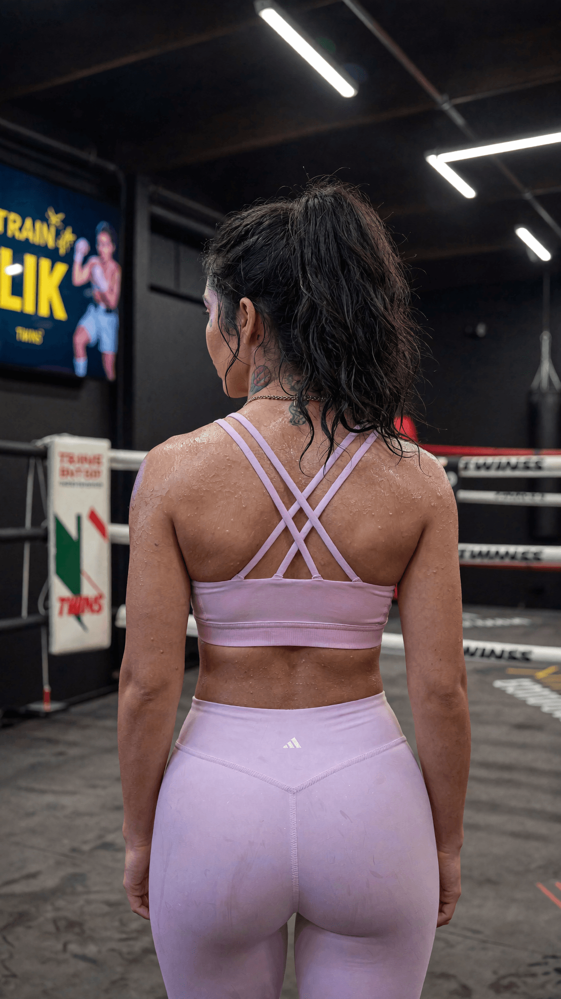 A woman in a pink athletic outfit stands confidently in a studio setting, with a focus on her full-body pose and attire.
