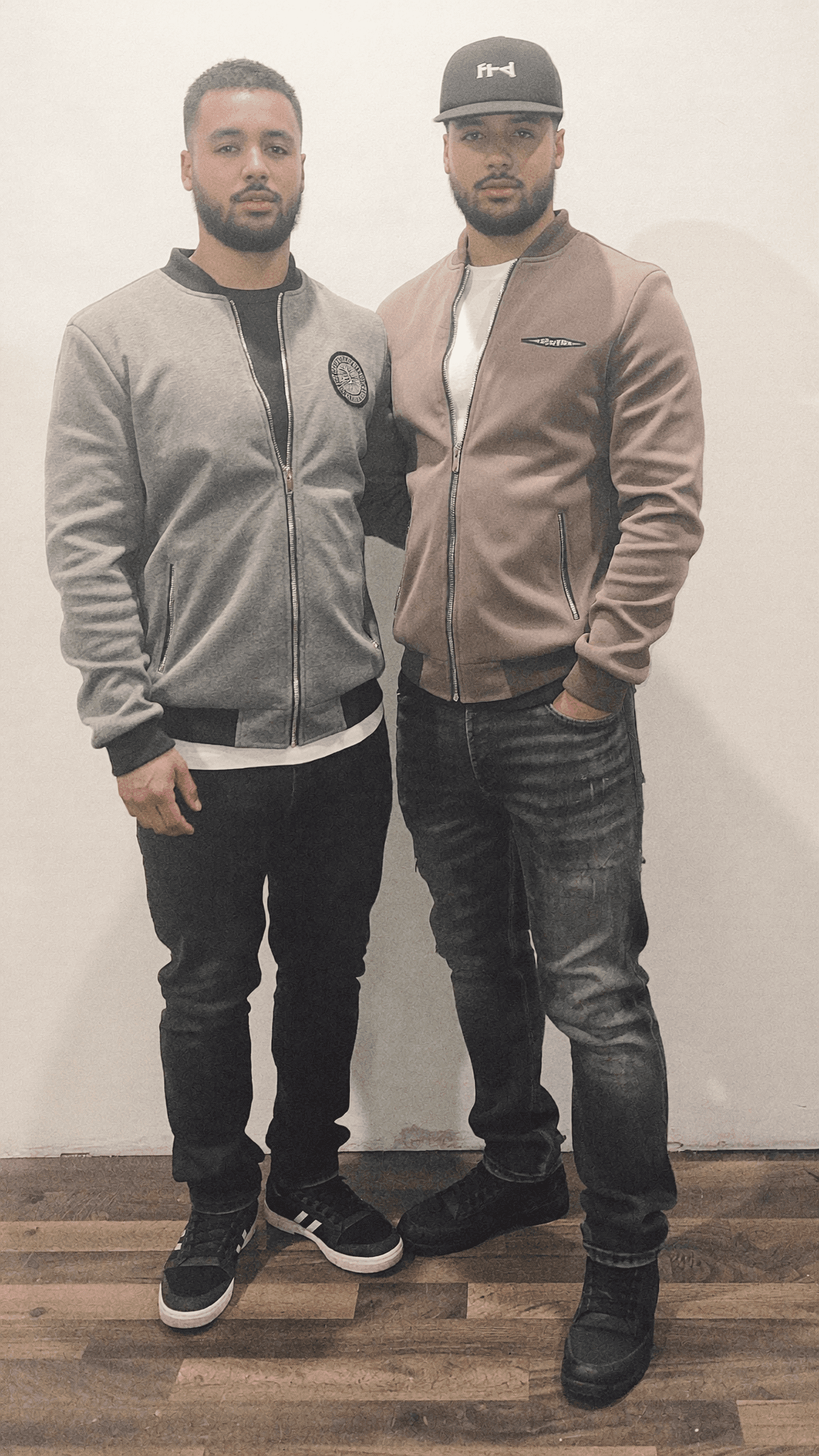 Two men stand side by side in a studio, dressed casually.