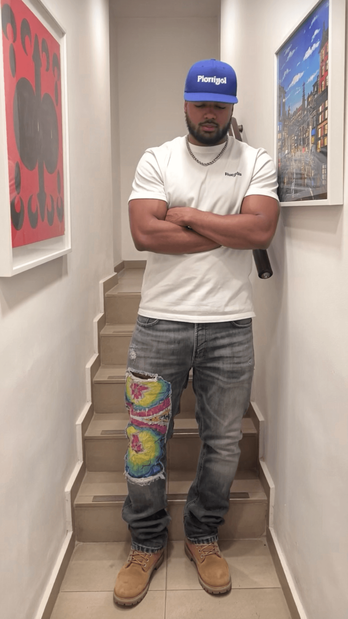 A man stands on stairs wearing casual clothing with a relaxed pose.