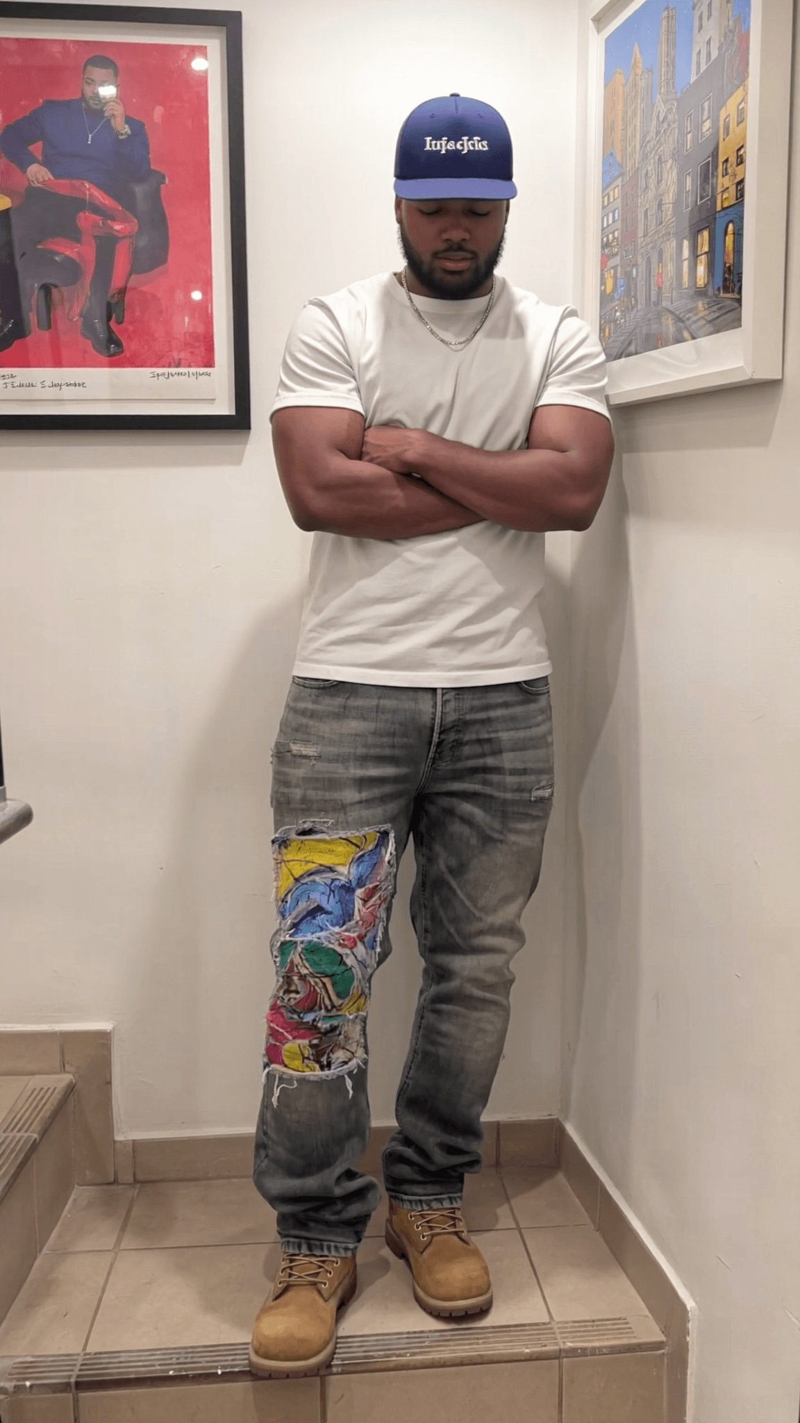 A man stands in a casual pose with arms crossed, wearing jeans and boots.