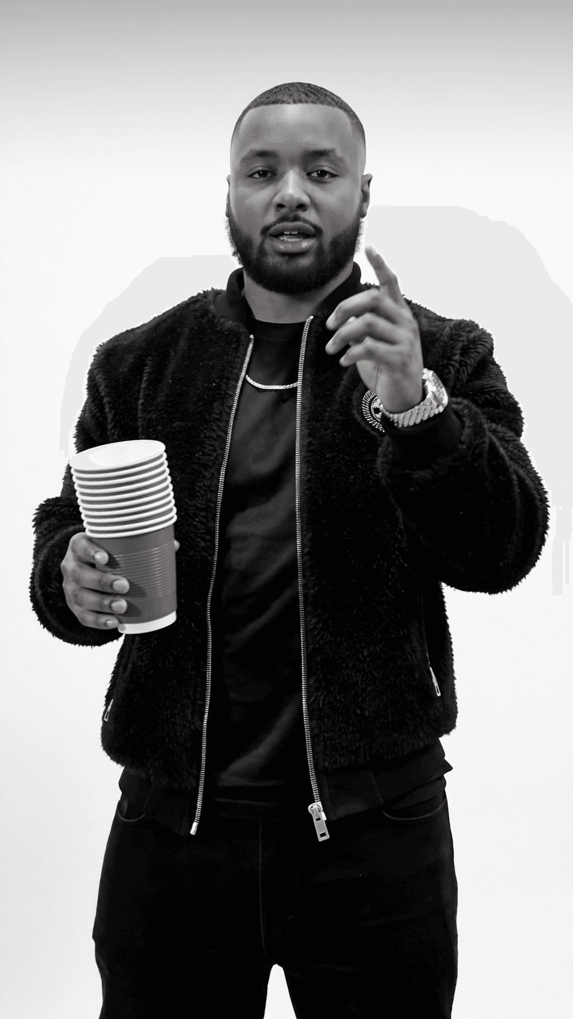 A person in casual attire holds a stack of cups while posing for the camera.