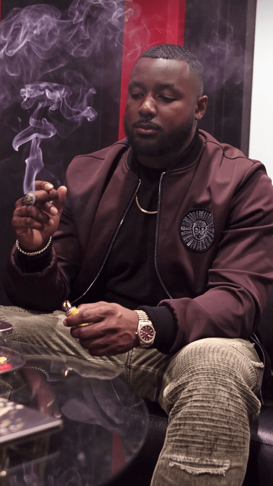 A man in casual attire is seated, holding a cigar and lighter.
