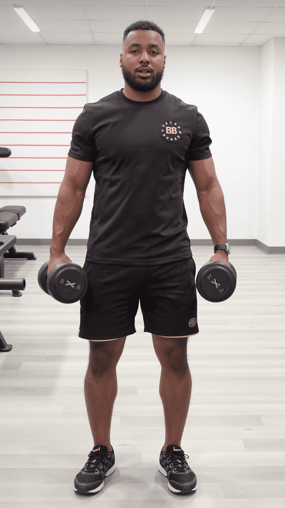 A man in an athletic outfit stands confidently holding dumbbells, ready for a workout.
