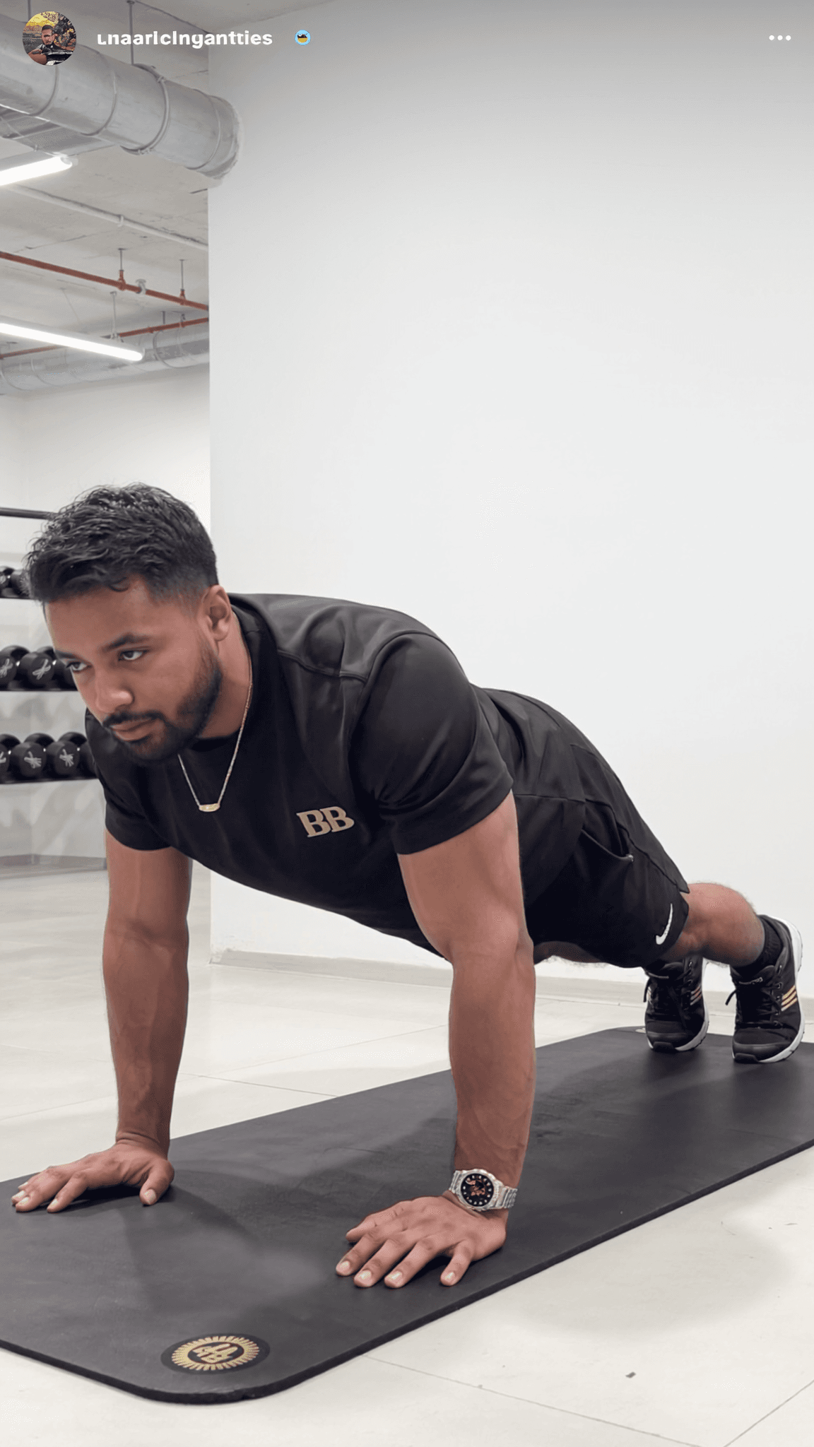 A man in an athletic outfit performs a prone exercise on a mat in a studio setting.