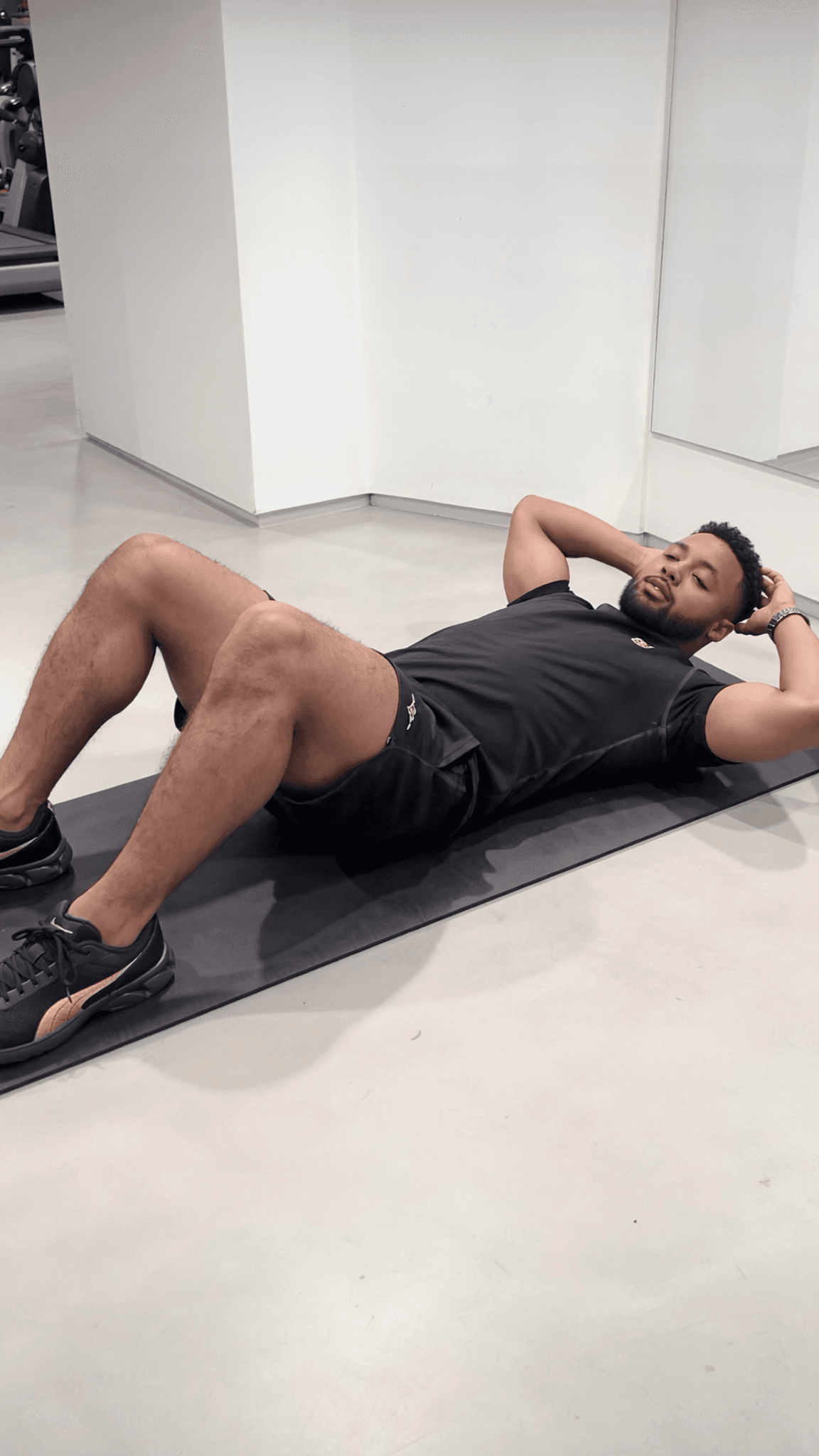 A man in an athletic outfit is performing a prone exercise on a mat in a studio setting.