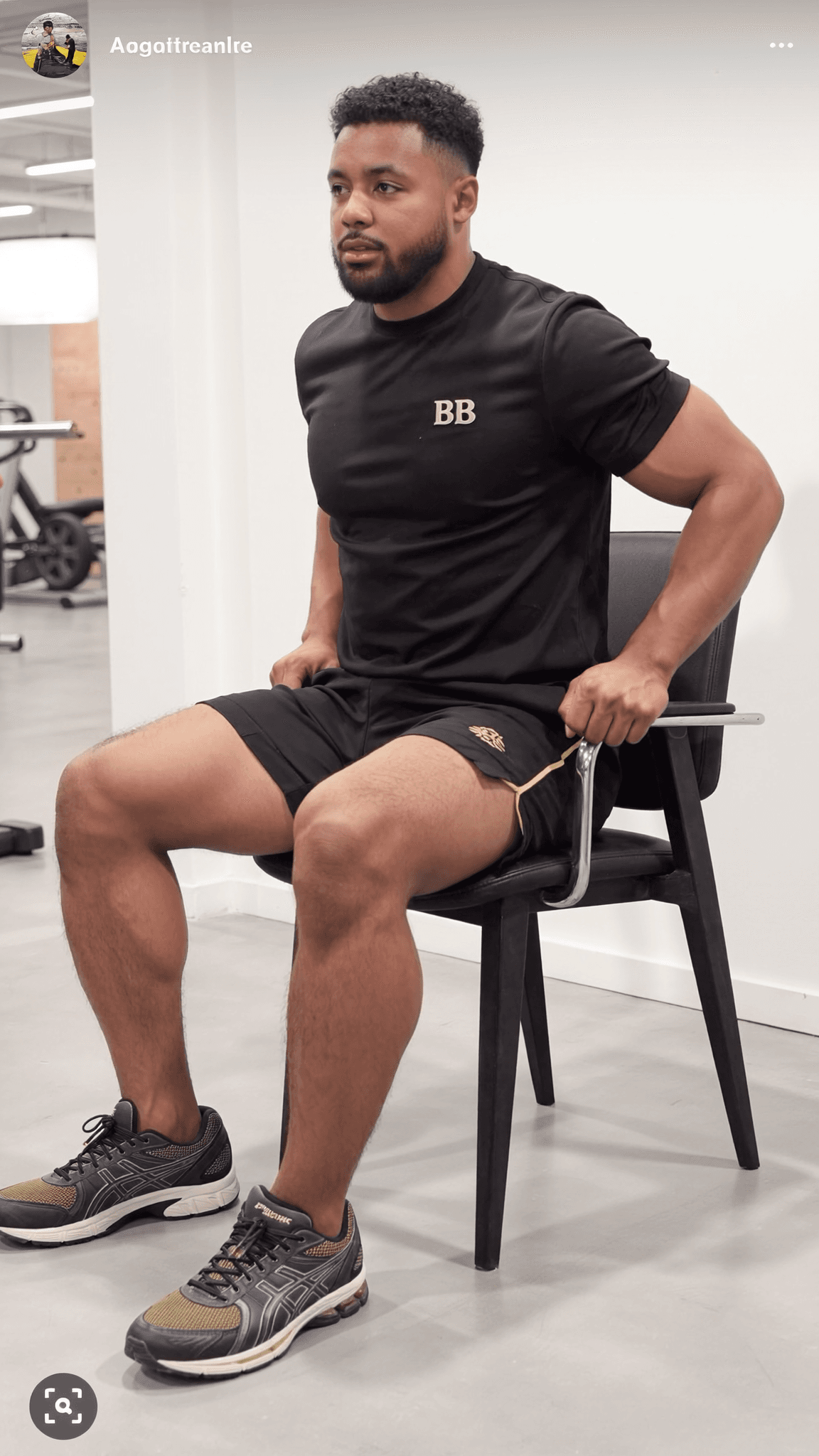 A muscular man in athletic wear sits on a chair, appearing focused and confident.