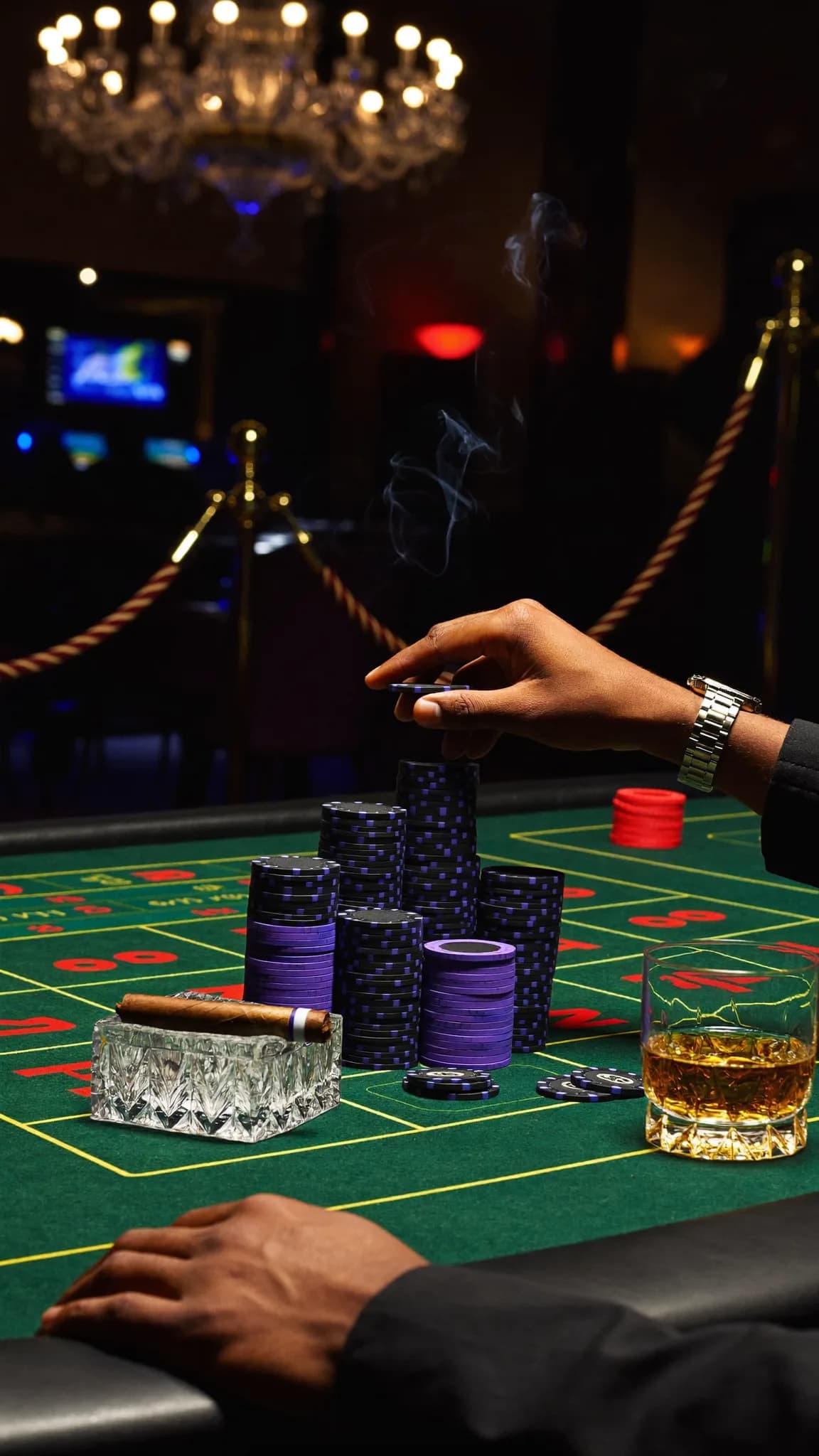 A person is seated at a casino table with poker chips and a cigar, holding a cigarette.
