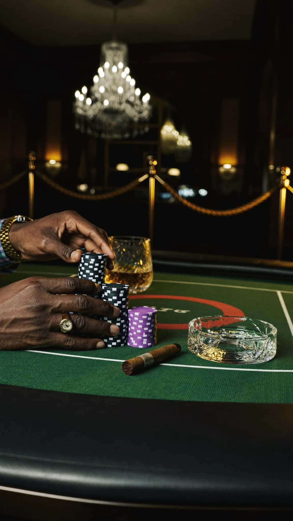 A person is seated at a casino table with poker chips and a cigar.