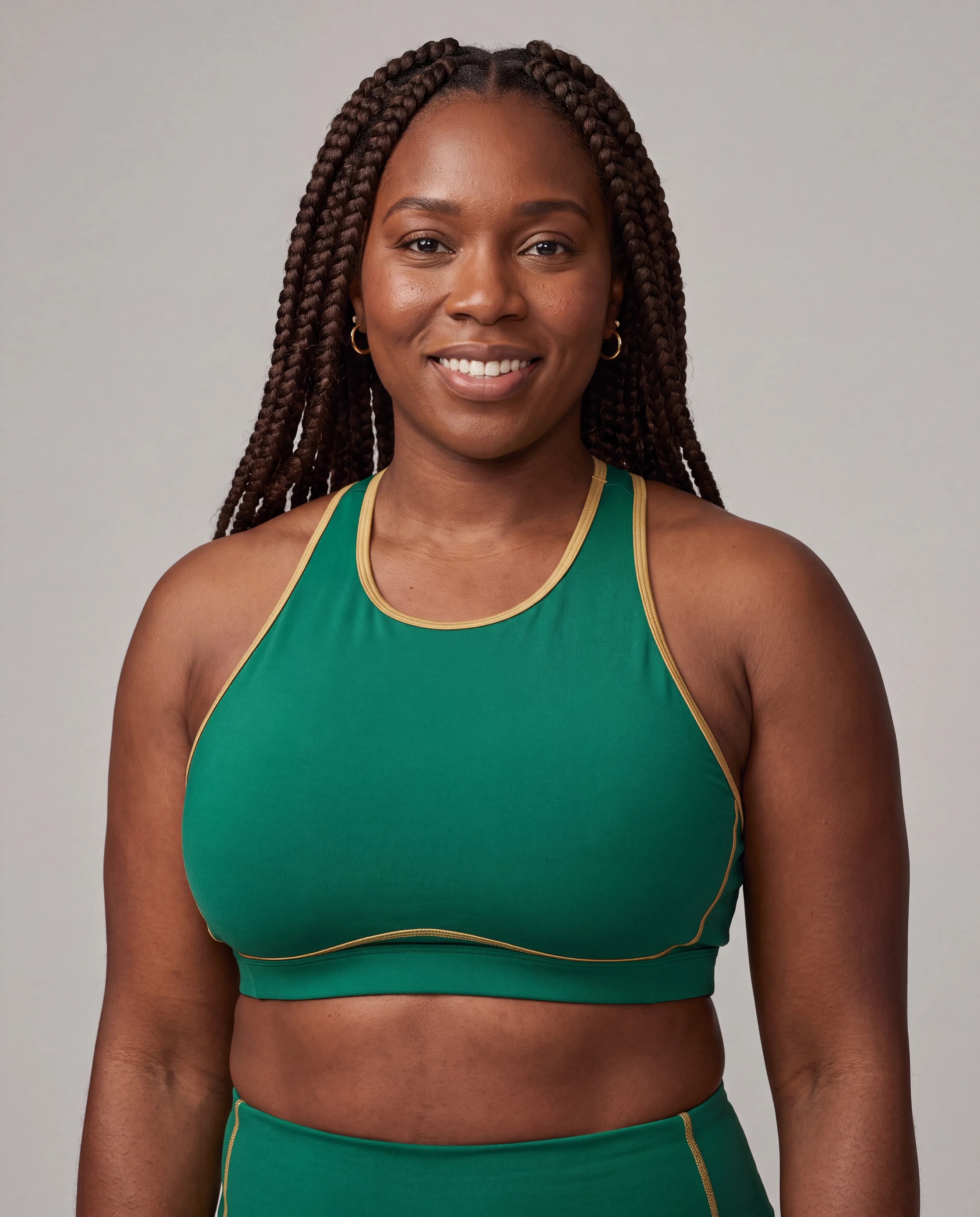 A woman with braided hair wearing a green sports bra and matching bottoms poses in a studio setting.