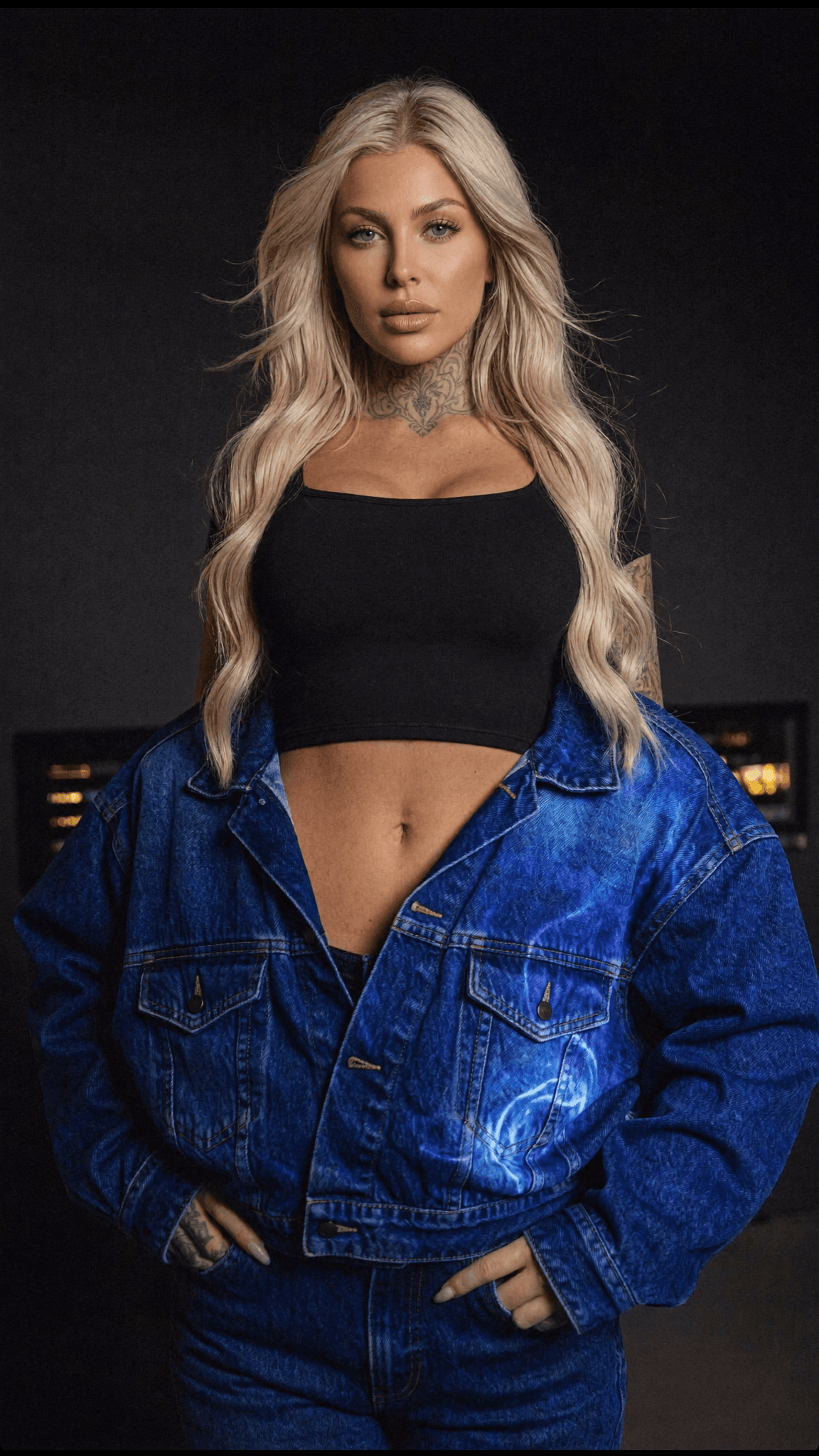 A woman with platinum blonde hair and a denim jacket poses confidently in a studio setting.